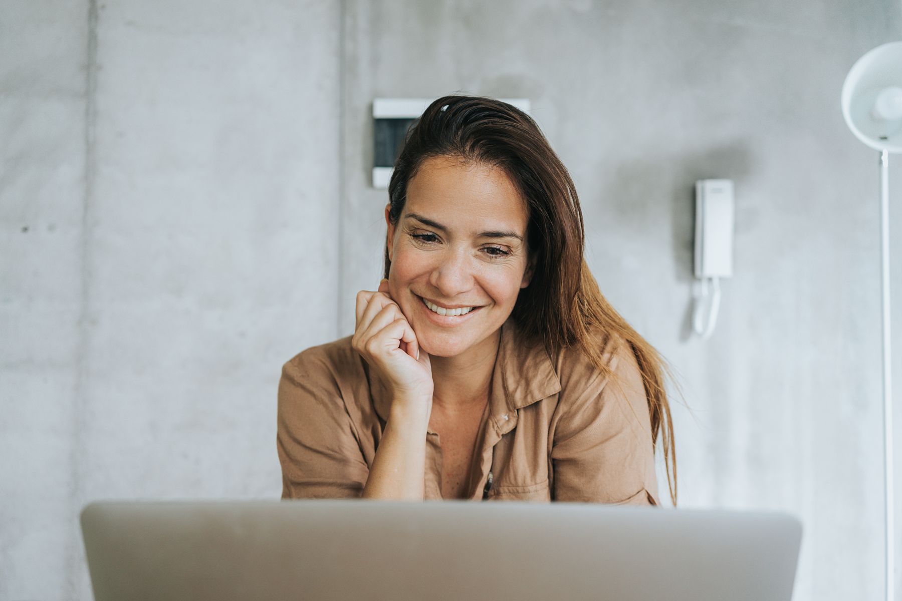 A woman smiling at her laptop in a bright room